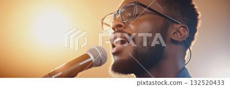 Close up of a young male singer passionately singing into a microphone on a stage, illuminated by warm, golden light, showcasing the energy and emotion of a live musical performance Close up of a young male singer passionately singing into a microphone on a stage, illuminated by warm, golden light, showcasing the energy and emotion of a live musical performance 132520433