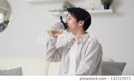 Asian man drinking protein in the living room Asian man drinking protein in the living room 132523971