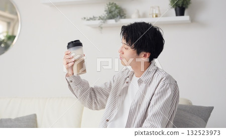 Asian man looking at protein shake in living room Asian man looking at protein shake in living room 132523973