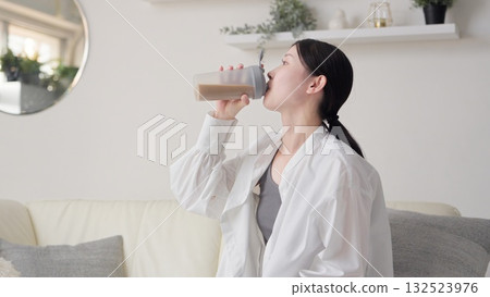 Asian woman drinking protein in the living room Asian woman drinking protein in the living room 132523976