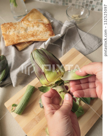 Anonymous person peels artichoke in kitchen at home. Healthy eating and traditional Italian dish. Fresh seasonal farm produce. Anonymous person peels artichoke in kitchen at home. Healthy eating and traditional Italian dish. Fresh seasonal farm produce. 132525097