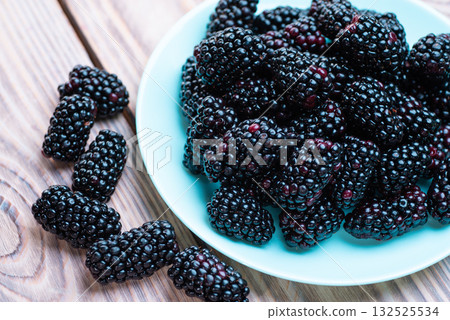 Large fresh blackberries in a plate on a wooden table 132525534