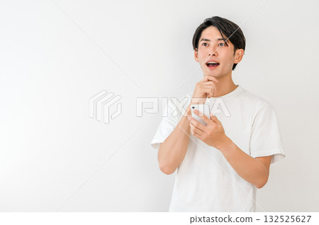 一位年輕的亞洲男子看著他的智慧型手機，突然靈光一閃（想法、創意、想像、構思、計畫） 132525627