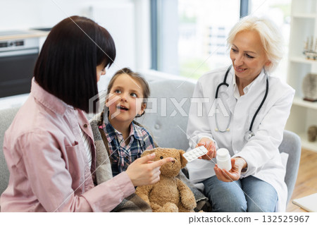 A female doctor is showing pills to a young girl and her mother, likely explaining the dosage and treatment plan for an illness. A female doctor is showing pills to a young girl and her mother, likely explaining the dosage and treatment plan for an illness. 132525967