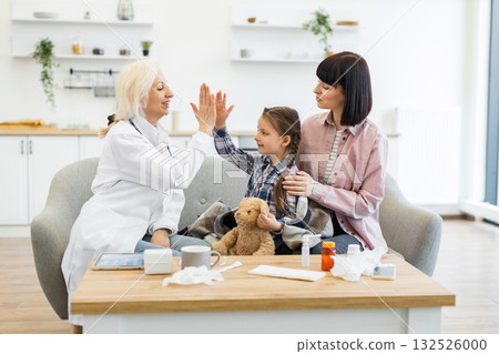 A doctor celebrates with a young girl after a checkup, with the mother present, creating a positive and reassuring atmosphere. A doctor celebrates with a young girl after a checkup, with the mother present, creating a positive and reassuring atmosphere. 132526000