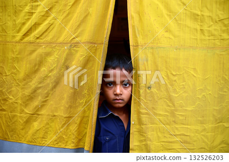 Curious Child Peeking Through a Yellow Curtain in a Vibrant Market Setting During the Day 132526203