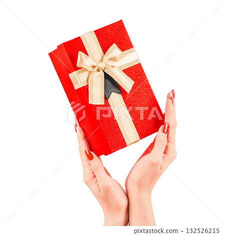 Female hands holding a red gift box with a golden ribbon and bow, isolated on white background. Elegant festive present concept for Christmas, New Year, or Valentine's Day 132526215