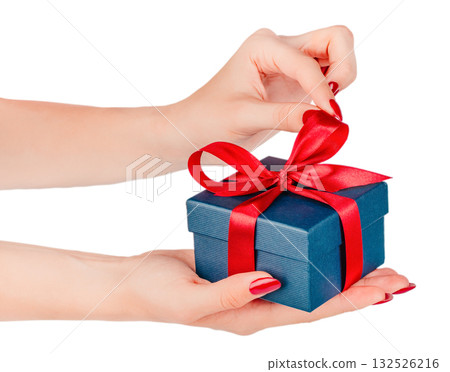Female hands opening a small dark blue gift box tied with a red satin ribbon, isolated on white background. Concept of surprise, holiday, or romantic present 132526216