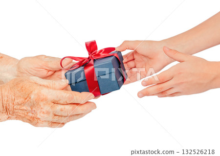 Close-up of elderly and young hands exchanging a blue gift box with a red ribbon, isolated on white. Symbolic concept of giving, care, gratitude, connection, family love between generations Close-up of elderly and young hands exchanging a blue gift box with a red ribbon, isolated on white. Symbolic concept of giving, care, gratitude, connection, family love between generations 132526218