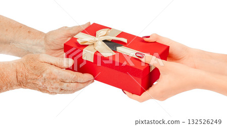 Elderly and young hands exchanging a red gift box with a gold ribbon and bow, isolated on white background. Concept of giving, love, care, generations, family connection, and holiday celebration Elderly and young hands exchanging a red gift box with a gold ribbon and bow, isolated on white background. Concept of giving, love, care, generations, family connection, and holiday celebration 132526249