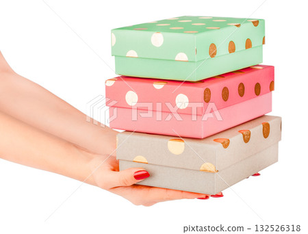 Female hands holding a stack of three colorful gift boxes with gold polka dots pastel green, pink, and beige packages isolated on white festive and cheerful concept birthday, Christmas celebration 132526318