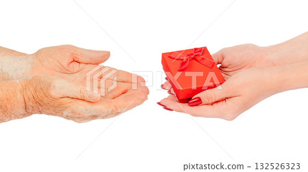 Young female hands offering a small red gift box with a bow to elderly hands waiting to receive it symbol of care, love, kindness, and intergenerational connection, isolated on white Young female hands offering a small red gift box with a bow to elderly hands waiting to receive it symbol of care, love, kindness, and intergenerational connection, isolated on white 132526323