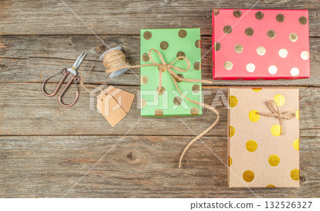 Colorful Christmas gift wrapping with golden polka dot boxes, twine, tags, and scissors on rustic wooden background with copy space Colorful Christmas gift wrapping with golden polka dot boxes, twine, tags, and scissors on rustic wooden background with copy space 132526327