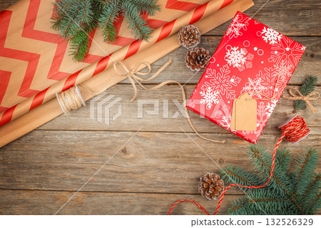 Festive Christmas gift wrapping with red snowflake paper, pine cones, twine, and craft supplies on rustic wooden background with copy space 132526329
