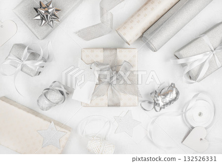 Stylish silver and white Christmas gift wrapping arrangement with ribbons, bows, and tags on light background, top view, festive flat lay 132526331