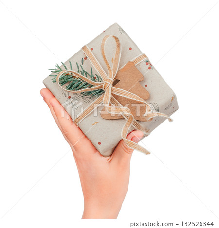 Hand holding small eco-friendly Christmas gift wrapped in kraft paper with pine twig, jute string, and wooden tree decoration minimal natural holiday packaging concept, isolated on white background Hand holding small eco-friendly Christmas gift wrapped in kraft paper with pine twig, jute string, and wooden tree decoration minimal natural holiday packaging concept, isolated on white background 132526344