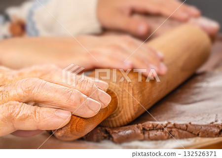 Close-up of elderly and young hands rolling gingerbread dough together, symbolizing generational connection, family tradition, and shared holiday moments Close-up of elderly and young hands rolling gingerbread dough together, symbolizing generational connection, family tradition, and shared holiday moments 132526371