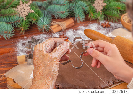 Generations connecting through holiday traditions elderly and young hands holding a gingerbread man cookie cutter over rolled dough, symbolizing family, love, and Christmas baking together. Generations connecting through holiday traditions elderly and young hands holding a gingerbread man cookie cutter over rolled dough, symbolizing family, love, and Christmas baking together. 132526383