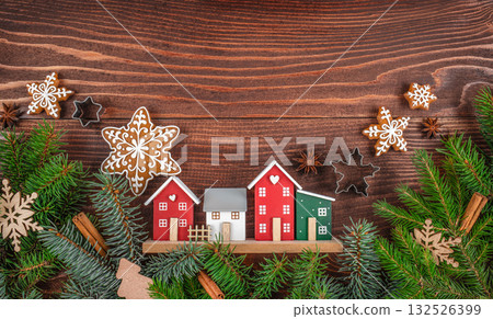 Cozy Christmas village scene with decorative houses, gingerbread snowflakes, fir branches, and festive spices on a rustic wooden background. copy space. top view Cozy Christmas village scene with decorative houses, gingerbread snowflakes, fir branches, and festive spices on a rustic wooden background. copy space. top view 132526399