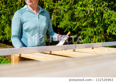 Woman painting a wooden pallet outdoors for a DIY project in her sunny tranquil backyard 132526963