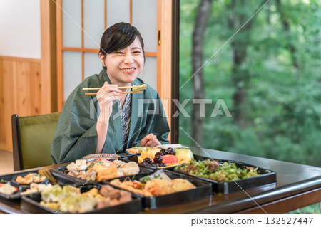 一位身穿浴衣的年輕女子正在津津有味地享用一桌食物。 一位身穿浴衣的年輕女子正在津津有味地享用一桌食物。 132527447