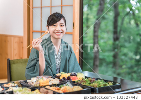 一位身穿浴衣的年輕女子正在津津有味地享用一桌食物。 一位身穿浴衣的年輕女子正在津津有味地享用一桌食物。 132527448