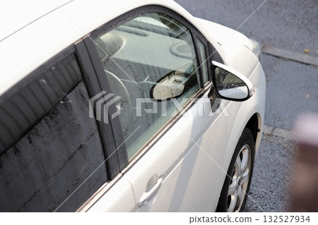 The driver's side of a white car parked in a parking lot on a rainy day 132527934