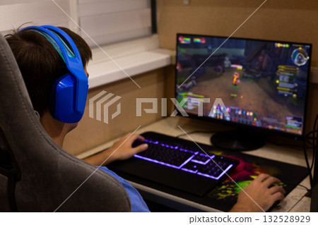 Person immersed in a digital world, playing a video game on a computer with modern equipment and vibrant headphones Person immersed in a digital world, playing a video game on a computer with modern equipment and vibrant headphones 132528929