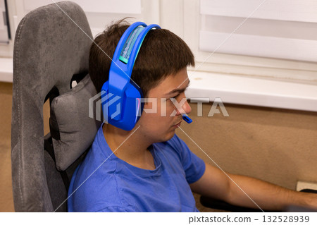 Digital meditation concept - gamer achieves flow state during intense gameplay. Blue headphones create sonic isolation, focused mind in comfortable gaming chair represents modern concentration 132528939
