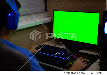 Back view gamer wearing headphones looking at green chroma key screen. Shoulder and side profile visible, perfect for adding custom background, composite image creation possibilities 132528940