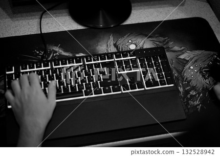 Black and white overhead view of keyboard with hand on WASD keys. Gaming mousepad on desk, moody atmosphere representing gaming addiction, frustration or negative aspects of video games Black and white overhead view of keyboard with hand on WASD keys. Gaming mousepad on desk, moody atmosphere representing gaming addiction, frustration or negative aspects of video games 132528942