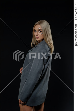 A young woman poses confidently in an oversized blazer on a dark backdrop A young woman poses confidently in an oversized blazer on a dark backdrop 132529096