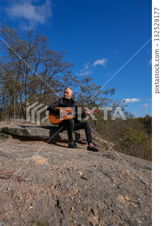 Blonde man playing string guitar outdoors in autumn forest. Concept of sound therapy, mental health and wellness rituals. Calmness tranquility audio-sensory practices. Aura farming energy 132529177