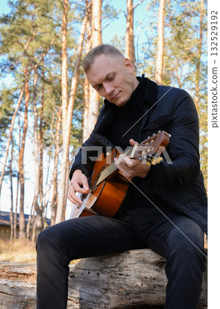 Beautiful blonde man playing acoustic guitar and singing relaxing enjoying outdoors on sunny autumn day. Artist learning and practicing playing musical instrument. Fall leaves autumnal Beautiful blonde man playing acoustic guitar and singing relaxing enjoying outdoors on sunny autumn day. Artist learning and practicing playing musical instrument. Fall leaves autumnal 132529192