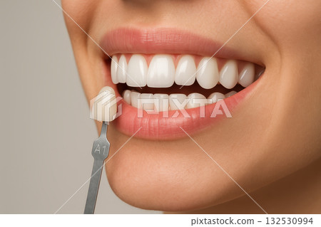 Close up of smile showing white teeth with veneer shade guide held next to teeth for color matching in dental veneer treatment enhancing bright and healthy appearance 132530994