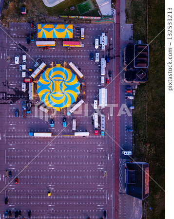 Aerial view of vibrant circus setup in parking lot blue yellow spiral tent surrounded by trailers and smaller tents, showcasing 132531213