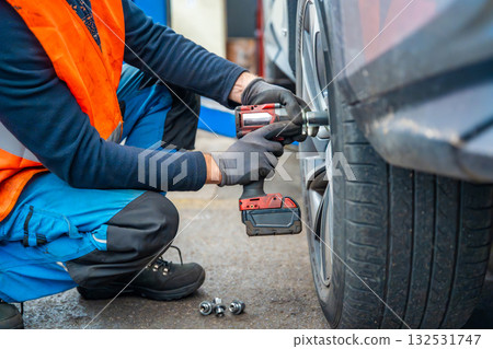 Mechanic using an impact wrench to remove lug nuts from a car wheel. Seasonal tire change and professional car service in preparation for winter. 132531747
