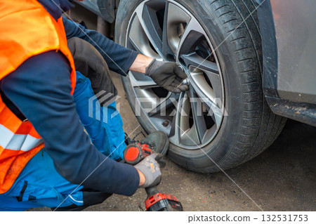Mechanic using an impact wrench to remove lug nuts from a car wheel. Seasonal tire change and professional car service in preparation for winter. 132531753