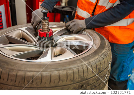 Car wheel positioned on a tire changing machine before removing the tire from the rim. Seasonal tire replacement process at an auto service during winter preparation. Car wheel positioned on a tire changing machine before removing the tire from the rim. Seasonal tire replacement process at an auto service during winter preparation. 132531771