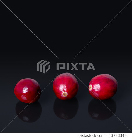 Cranberries in a row, front view and close-up, on a black glass plate. Fresh and ripe, intense red, large cranberries, fruits of Vaccinium macrocarpon, also called bearberries, and American cranberry. 132533493