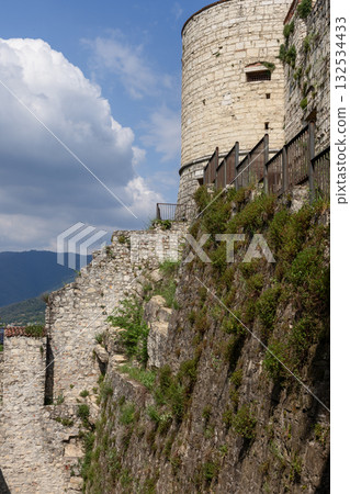 Torre Coltrina of Brescia Castle rises above limestone walls and Strada del Soccorso passage 132534433