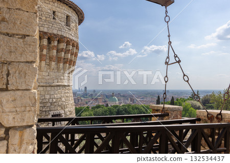 View from Brescia Castle drawbridge toward sunny cityscape framed by Prisoners Tower and chains 132534437