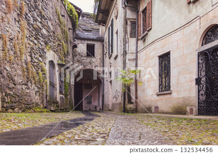 Narrow stone alley on San Giulio Island with moss-covered walls and iron gates under soft light 132534456