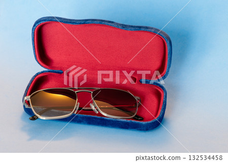 Stylish eyewear placed in red lined velvet case with blue exterior on gradient blue backdrop 132534458