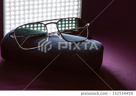 Elegant tinted sunglasses placed on velvet case with dramatic light on magenta surface 132534459
