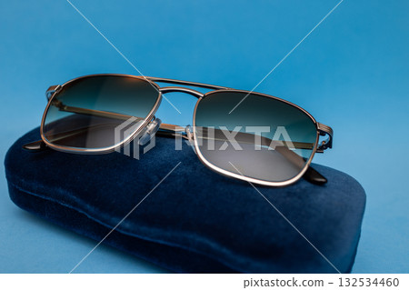 Elegant composition of stylish metallic sunglasses placed on deep blue velvet under studio light 132534460