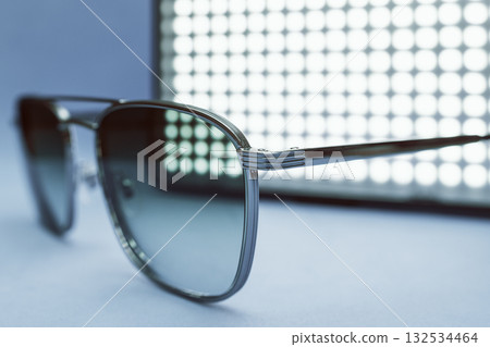 Futuristic eighties revival sunglasses placed before glowing LED grid on soft blue surface Futuristic eighties revival sunglasses placed before glowing LED grid on soft blue surface 132534464