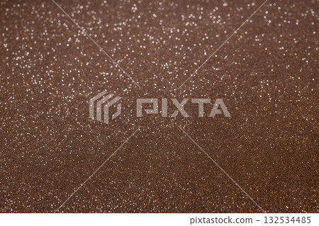 Brown glitter texture glowing under light with granular details below and blurred sparkles above 132534485