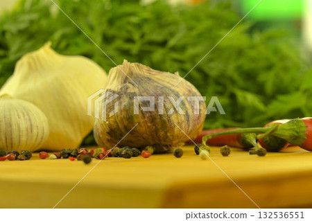 The bulbs of garlic, red chili peppers, four-color pepper, and carrot tops on a wooden cutting board. The concept of culinary arts and vegetables in the home. Macro image, close-up. Garlic - species The bulbs of garlic, red chili peppers, four-color pepper, and carrot tops on a wooden cutting board. The concept of culinary arts and vegetables in the home. Macro image, close-up. Garlic - species 132536551