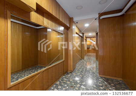 A modern hallway with wooden paneling and polished stone flooring. The space is well-lit with ceiling lights and features large mirrors on the walls. 132536677